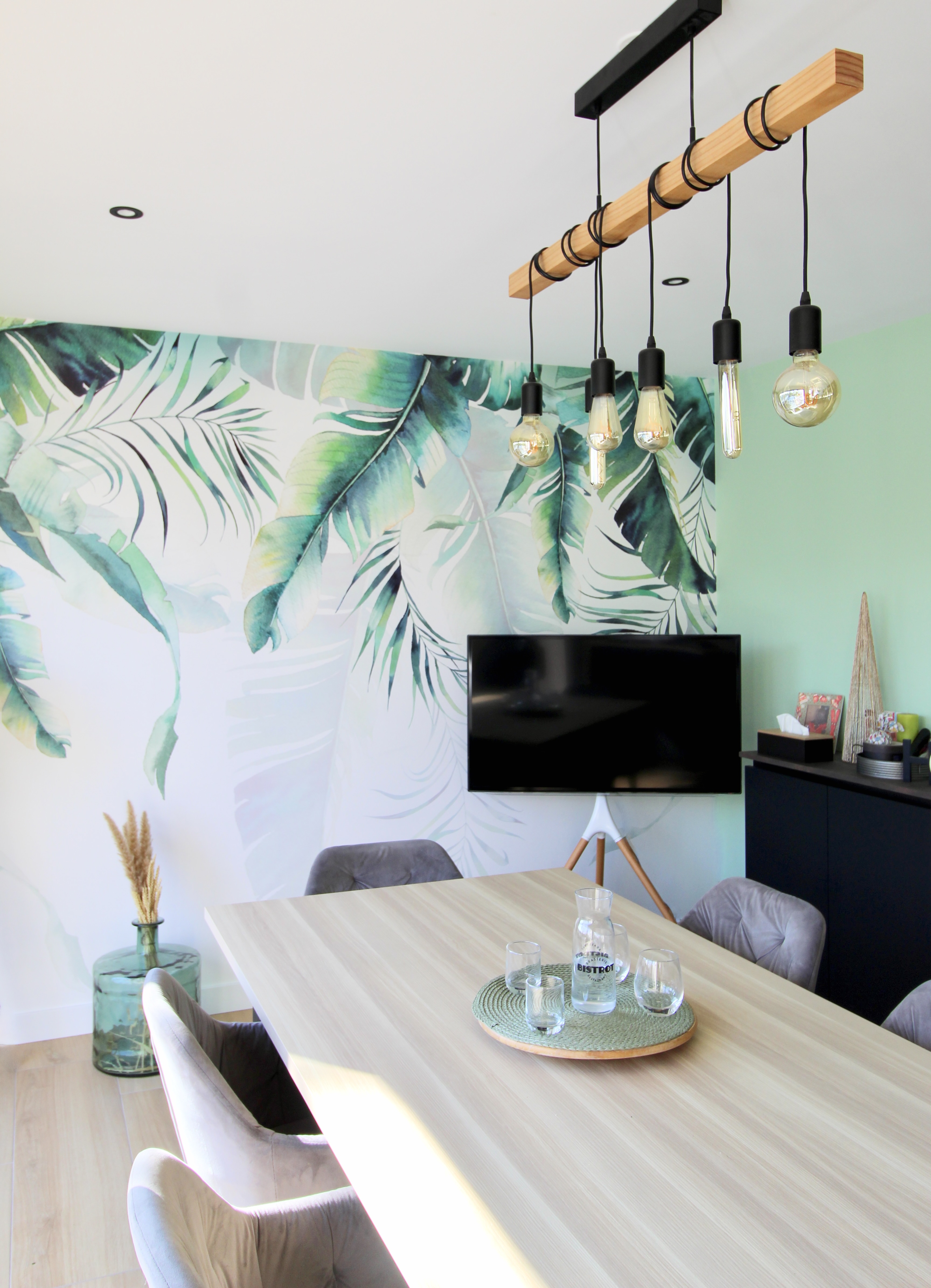 Salle à manger moderne avec papier peint feuillage tropical et suspension design en bois et ampoules apparentes