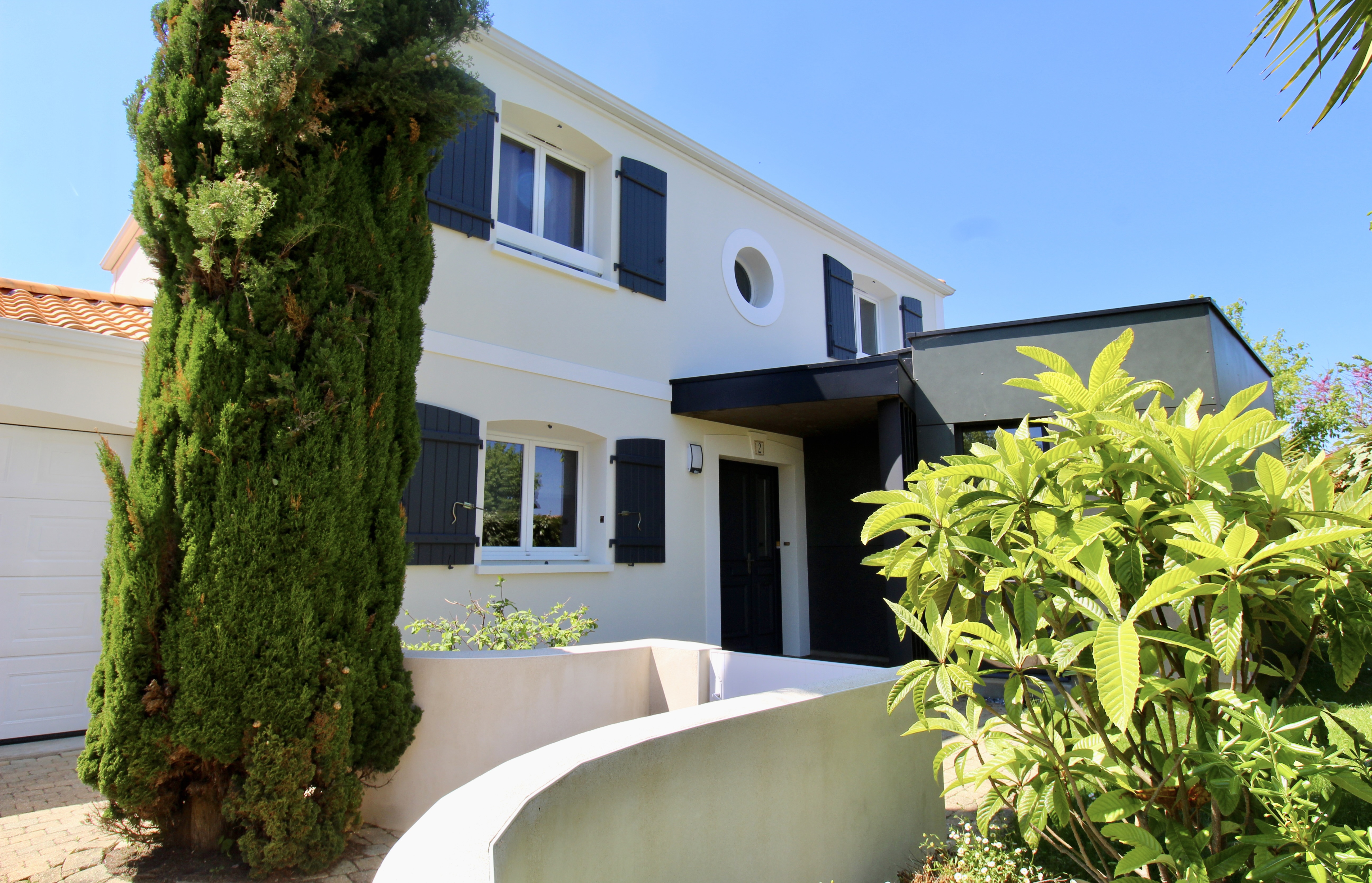 Maison contemporaine blanche avec volets noirs et jardin verdoyant rénové vue de loin