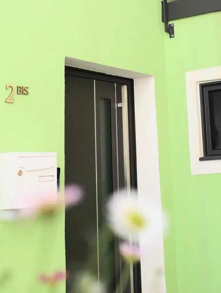 Entrée de maison moderne à façade verte avec porte vitrée et boîte aux lettres blanche