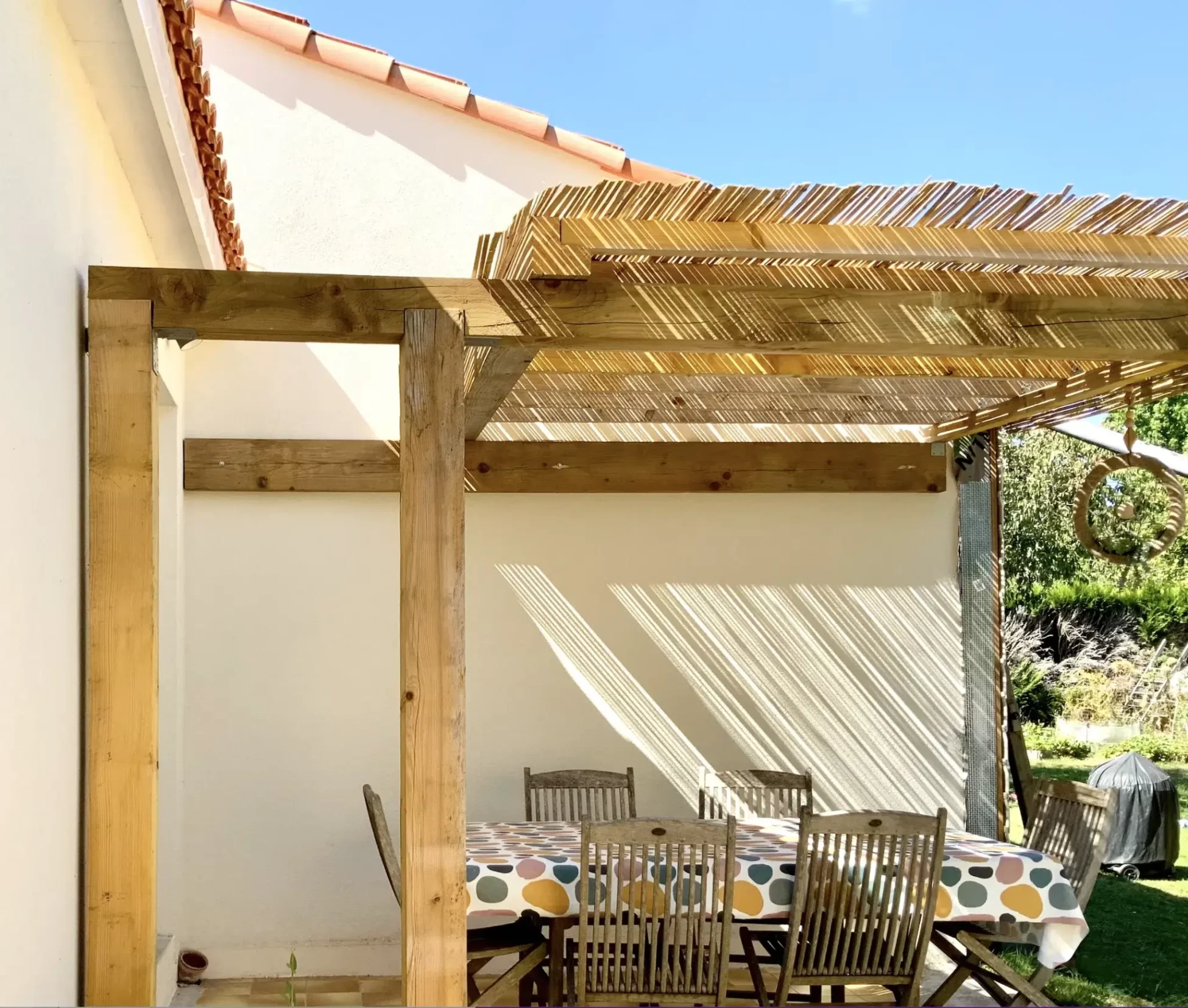 Terrasse extérieure avec pergola en bois et table de jardin couverte d’une nappe colorée