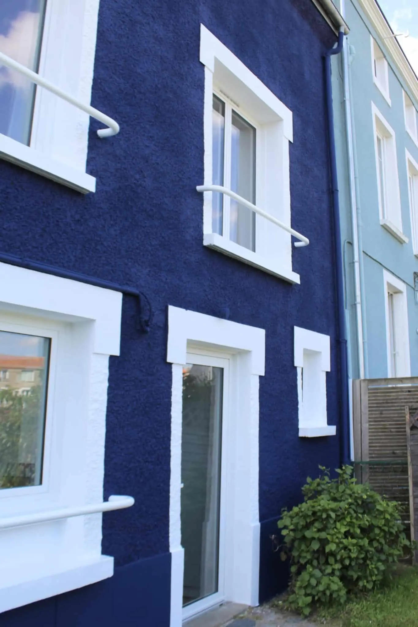 Façade de maison bleue avec encadrements de fenêtres blancs et porte vitrée après rénovation